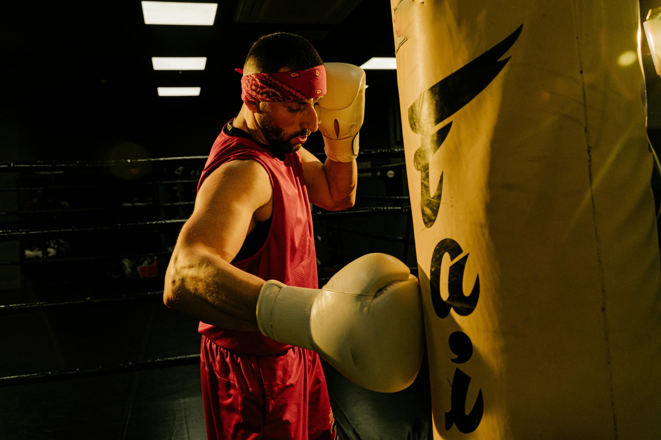 Focused male boxer in red bandana training intensely with a punching bag in a gym.