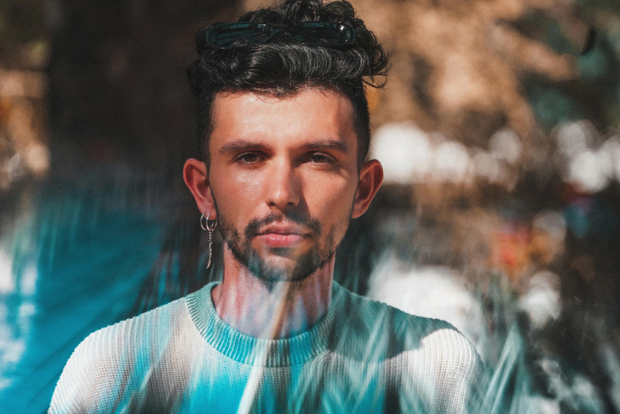 Stylish young man with earring in a sunlit urban setting, showcasing modern fashion.